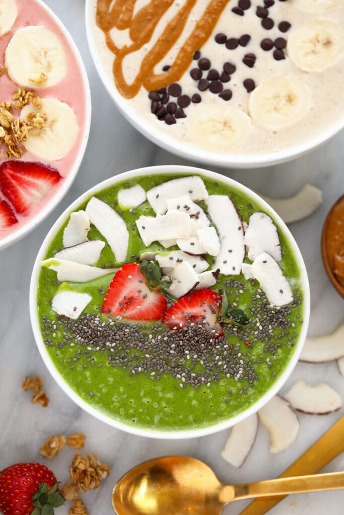 Green smoothie bowls are a great way to eat your breakfast and your greens too! This recipe is made with our favorite green smoothie recipe and sneaks in nutrient-dense foods like avocado, spinach, and cauliflower, but we promise you can't taste them. green smoothie bowl with strawberries, coconut, and chia seeds