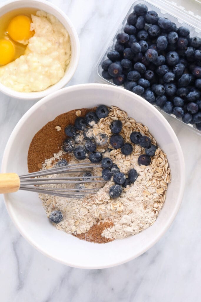 These Blueberry Oatmeal Muffins are super fluffy and made with a short list of healthy ingredients. Plus, they pack 3g of protein per muffin. Enjoy! blueberry oatmeal muffin ingredients in a bowl, ready to be mixed together