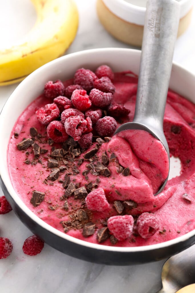 This 5-ingredient Raspberry Chocolate Chunk Nice Cream boasts the same creamy deliciousness of traditional raspberry ice cream, but without all those fillers. raspberry chocolate chunk banana nice cream in a bowl being scooped with an ice cream scooper