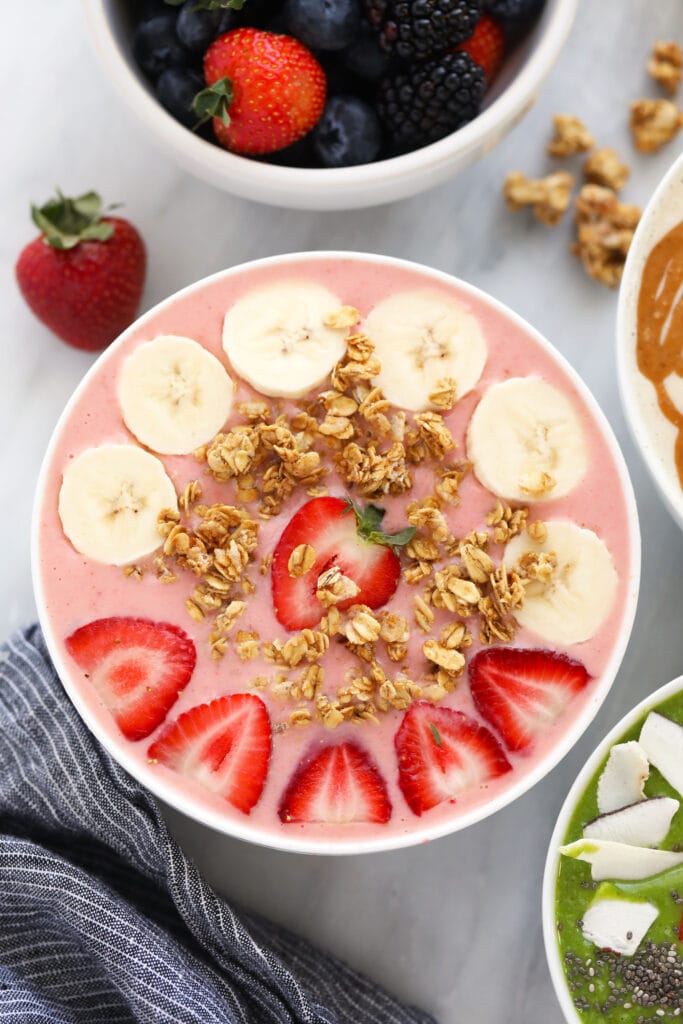 This Strawberry Smoothie Bowl is made with our classic Strawberry Smoothie and I know you will just adore it. All you need are 5 ingredients and then delicious toppings such as granola, fresh strawberries, and bananas. strawberry smoothie with banana slices, granola, and strawberries