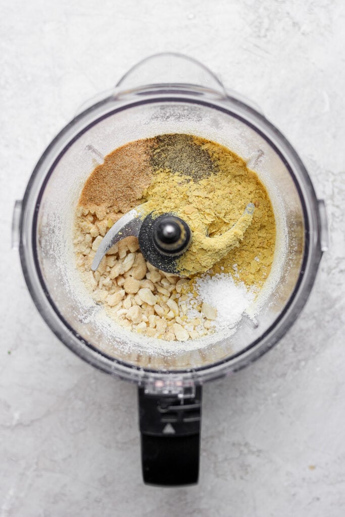 This 5-Ingredient Vegan Parmesan Cheese is a delicious vegan alternative to traditional grated parmesan. Make a batch and sprinkle onto any savory dish your heart desires. vegan parmesan cheese in a food processor about to be blended