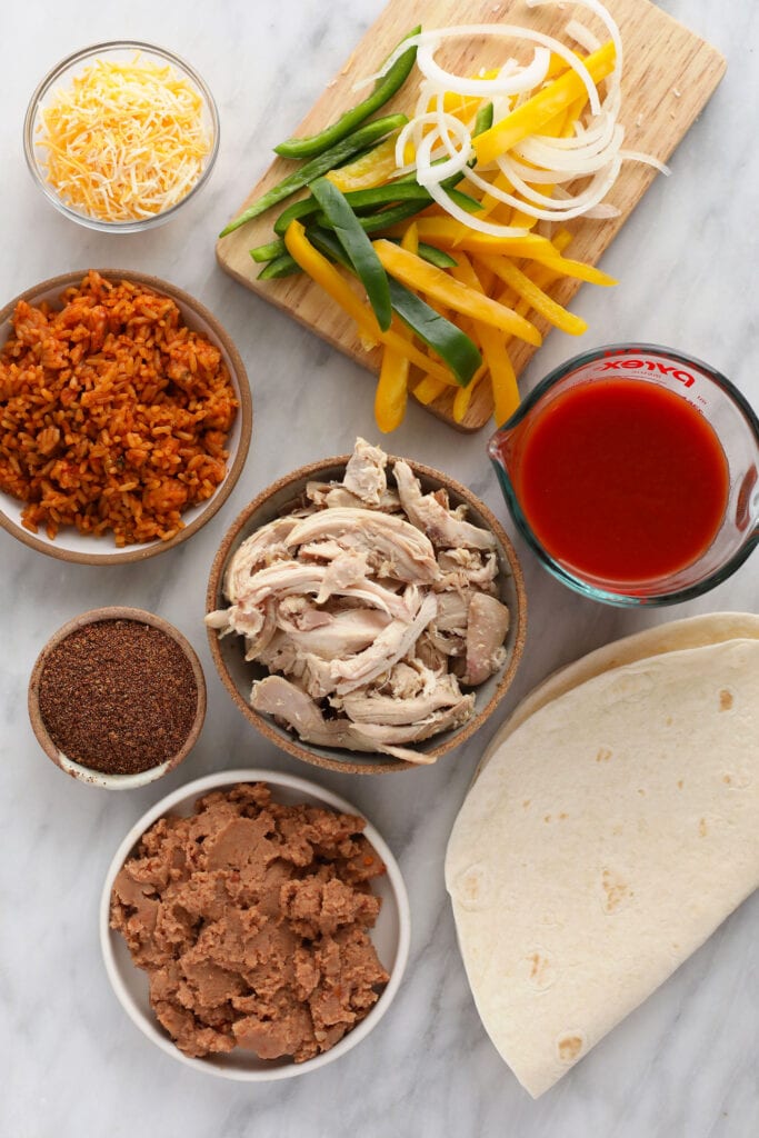 These easy shredded chicken burritos are super flavorful with smothered chicken and fajita veggies, refried beans and Spanish rice. Make a batch and enjoy immediately, or follow our freezer instructions for the ultimate meal prep recipe! ingredients for shredded chicken burritos, ready to be assembled