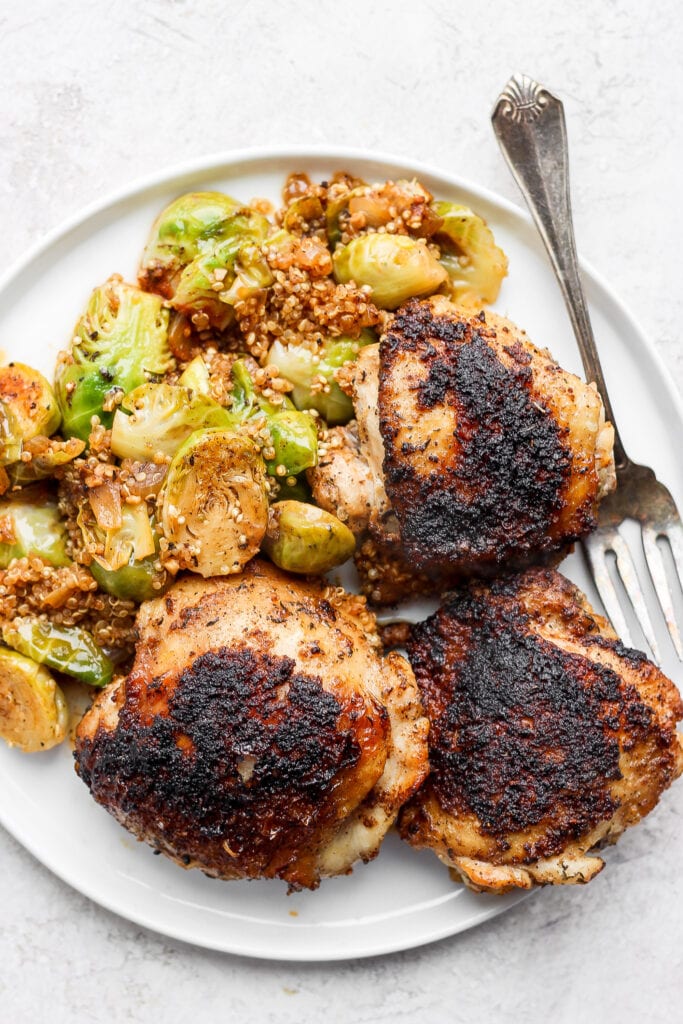 Perfectly cooked Dutch Oven Chicken Thighs made with Brussels sprouts and quinoa. This one-pot meal is packed with savory flavors and is made in only one pot! chicken thighs, Brussels sprouts, and quinoa on plate