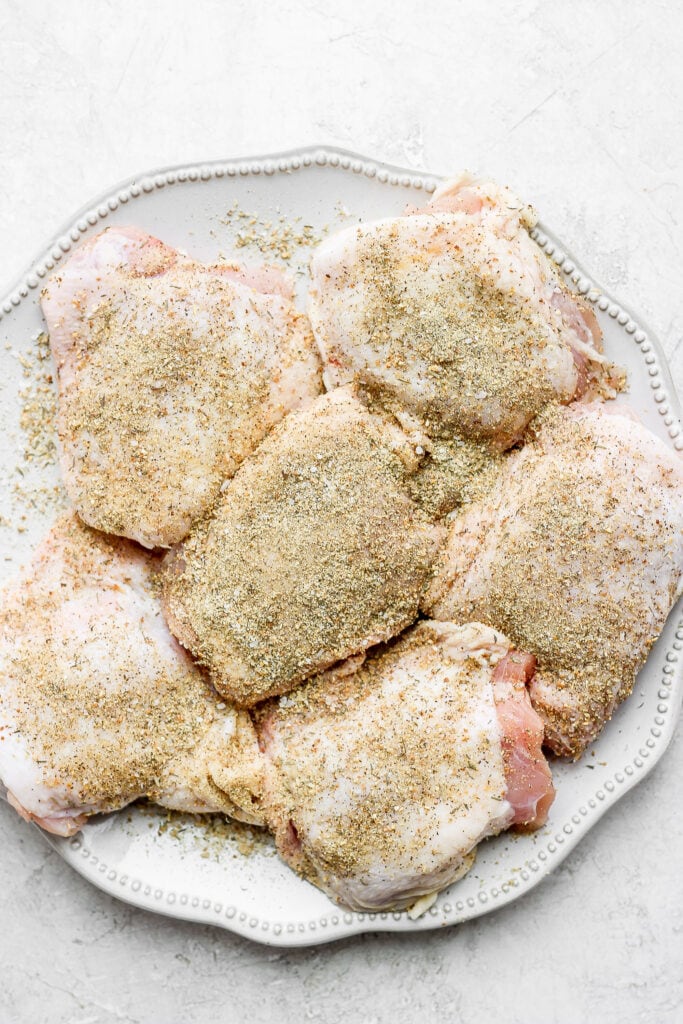 These Dutch Oven Chicken Thighs are seasoned with delicious spices, seared, and then cooked with quinoa and Brussels sprouts for a healthy one-pot meal. seasoned chicken thighs on plate