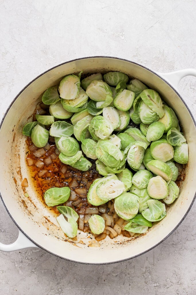 Perfectly cooked Dutch Oven Chicken Thighs made with Brussels sprouts and quinoa. This one-pot meal is packed with savory flavors and is made in only one pot! uncooked Brussels sprouts and onion in Dutch oven