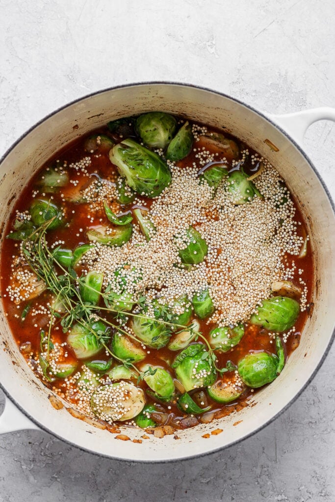Perfectly cooked Dutch Oven Chicken Thighs made with Brussels sprouts and quinoa. This one-pot meal is packed with savory flavors and is made in only one pot! Brussels sprouts, uncooked quinoa, and broth in Dutch oven