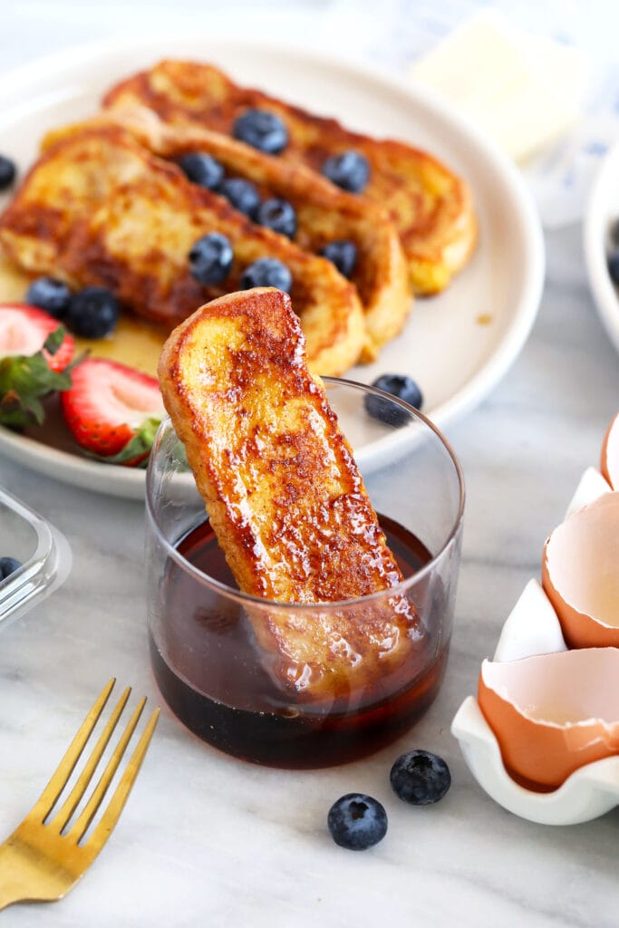 French Toast Sticks are an easy, kid-friendly breakfast recipe made with sliced brioche bread, egg, milk, and a cinnamon-sugar topping. french toast stick in a cup of maple syrup