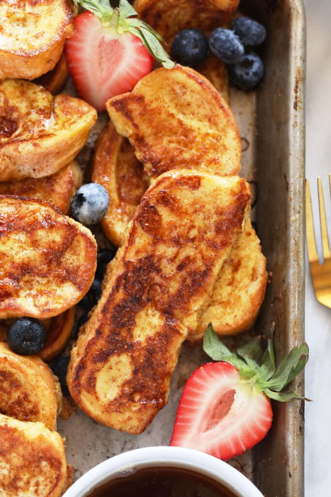 French Toast Sticks are an easy, kid-friendly breakfast recipe made with sliced brioche bread, egg, milk, and a cinnamon-sugar topping. French toast sticks on a baking sheet with strawberries
