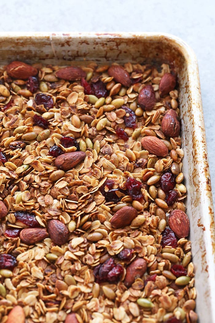 This crunchy, delicious homemade granola recipe is made with rolled oats, almonds, dried cranberries, and maple syrup. Granola on a baking sheet