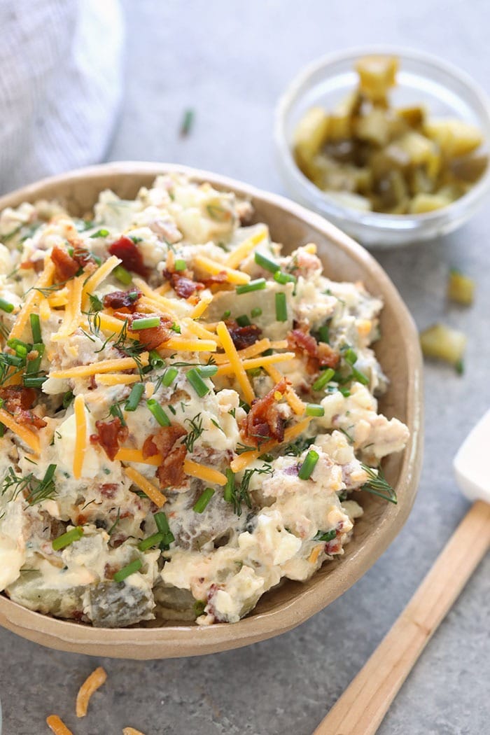 This baked potato salad recipe is loaded with cheddar cheese, hard boiled eggs, bacon, chives, and a delicious dill pickle sauce! loaded baked potato salad in a bowl