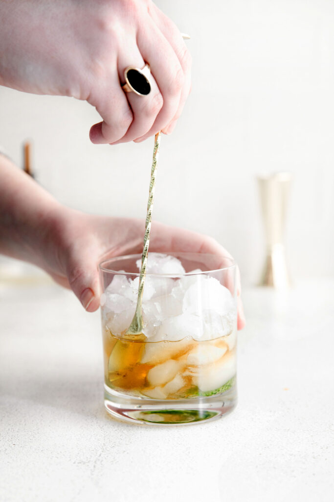 bourbon being stirred into a glass of ice with muddled mint for a mint julep