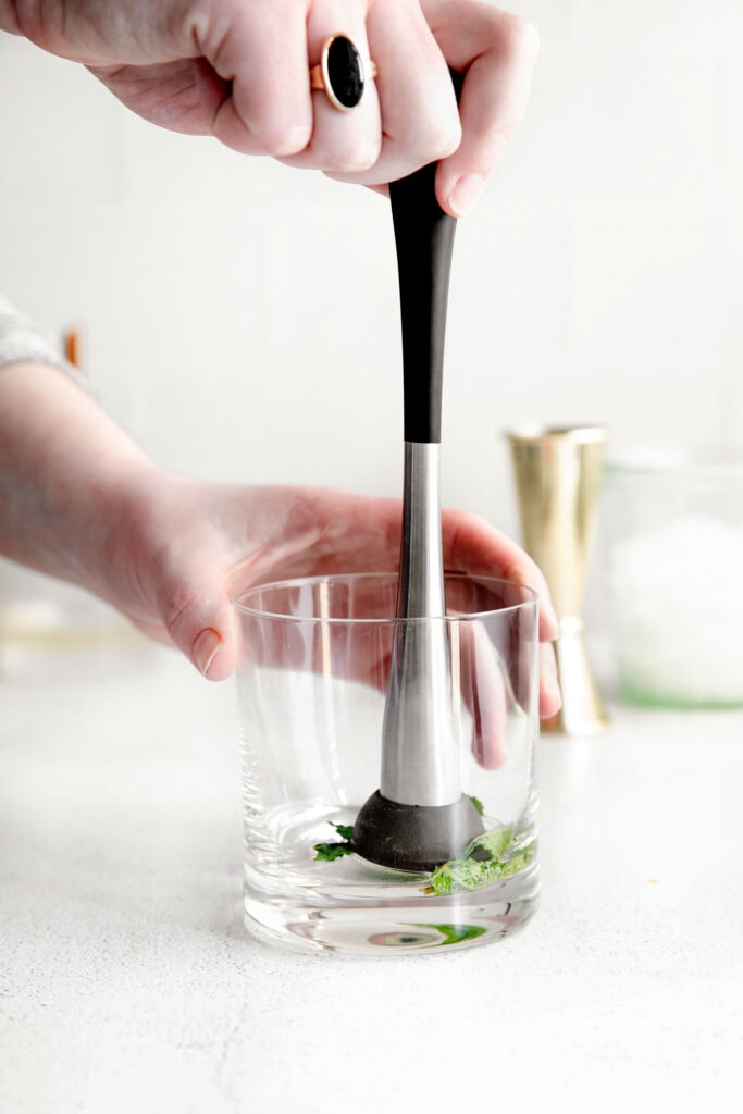 mint being muddled in the bottom of a glass for mint juleps