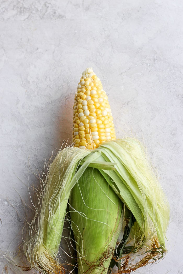 Take dinner up a notch and add this Mexican Street Corn Salad to the menu! This delicious healthy side dish is made with grilled corn, fresh veggies, and the most delicious cotija yogurt sauce. Drop everything you're doing and make this Mexican Street Corn Salad today! Half shucked corn on the cob.