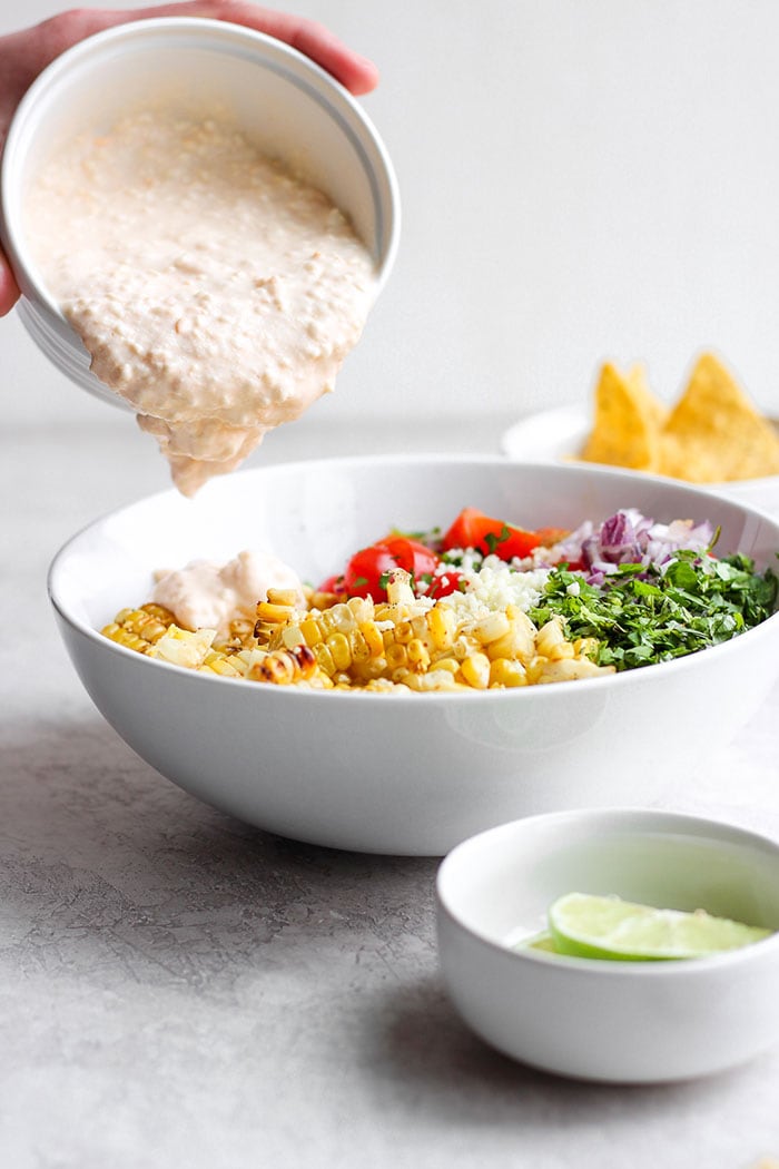 Take dinner up a notch and add this Mexican Street Corn Salad to the menu! This delicious healthy side dish is made with grilled corn, fresh veggies, and the most delicious cotija yogurt sauce. Drop everything you're doing and make this Mexican Street Corn Salad today! Pouring sauce onto the Mexican Street Corn Salad