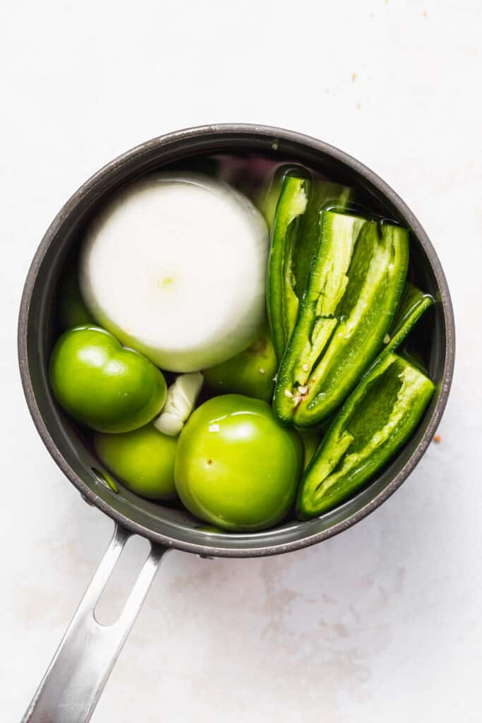Tomatillos, garlic, onion, jalpe&ntilde;os, and other ingredients in a saucepan. 