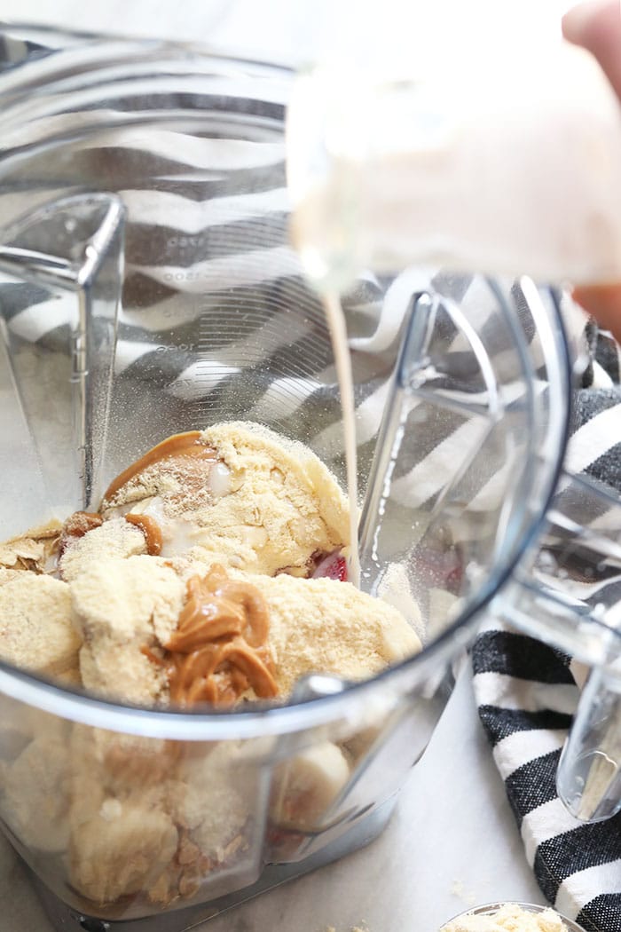 Start your day off right with this protein-packed healthy breakfast smoothie. Filled with fruit, oats, protein powder, almond milk and a little hit of peanut butter, this breakfast smoothie of all breakfast smoothies will keep you feeling satisfied til lunch. healthy breakfast smoothie ingredients being poured in the Vitamix