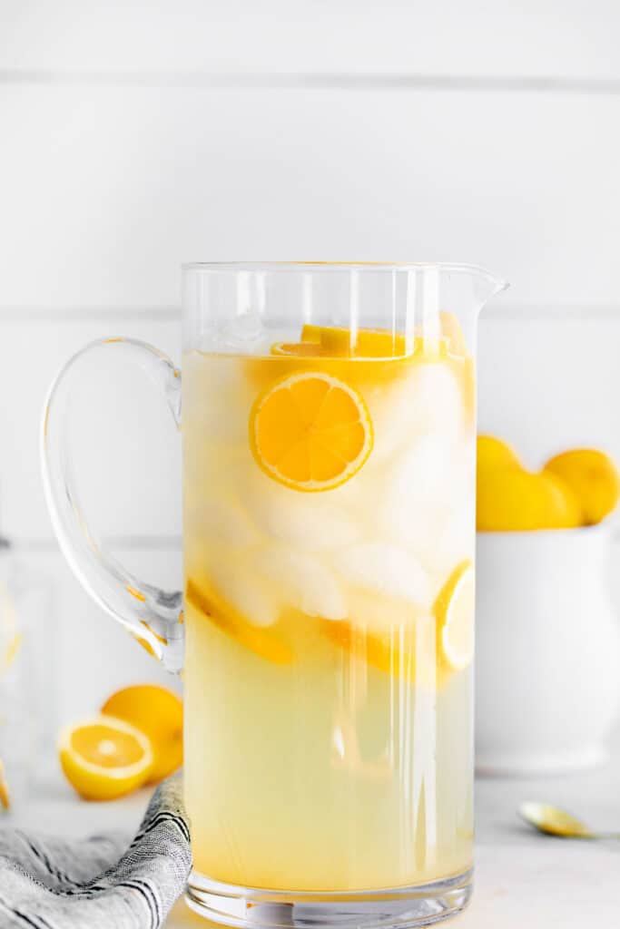 A pitcher of lemonade with ice and lemon slices floating in it.