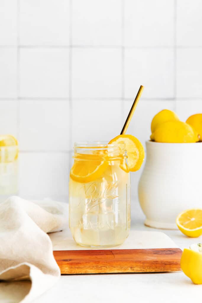 A jar of lemonade with a straw and lemon slices.