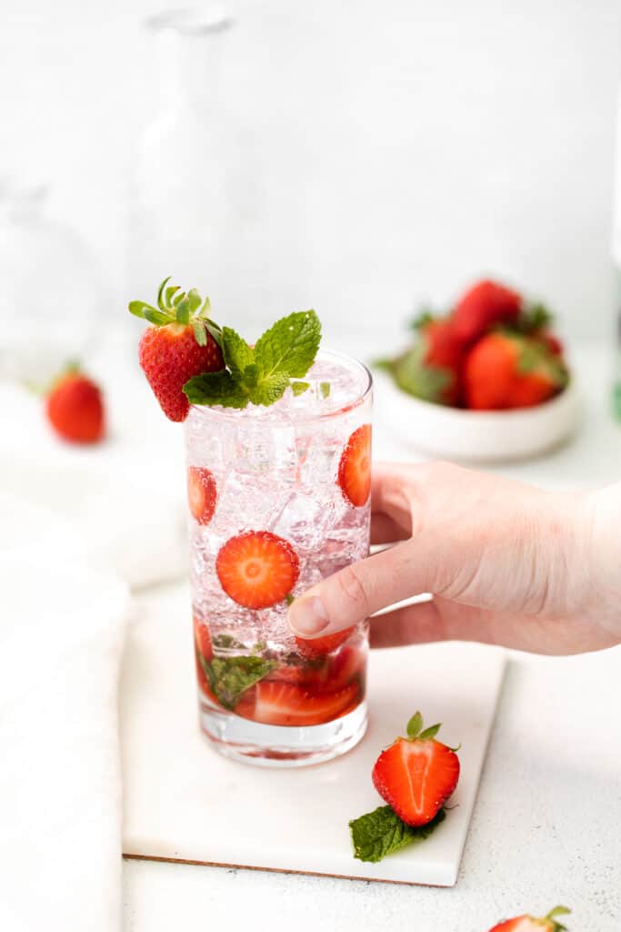 Fancy up your rum cocktail recipes with this strawberry mojito recipe! It's made with strawberries, mint, white rum, club soda, and a homemade mint simple syrup. hand holding strawberry mojito