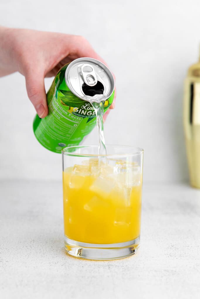A refreshing virgin margarita recipe that's made with lime juice, orange juice, a little agave nectar, and sparkling water. pouring sparkling water into a virgin margarita