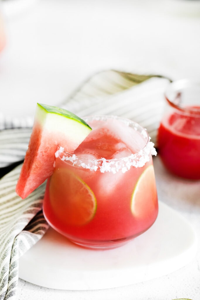 Watermelon margarita in a glass with a salted rim, lime rounds, and fresh watermelon.