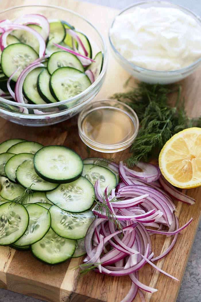 If you are looking for a healthy side salad for your next BBQ or a healthy salad for meal prep, look no further! This creamy cucumber salad is simple, flavorful, and delicious. Cucumber, red onion, apple cider vinegar, Greek yogurt, fresh dill, and lemon on a cutting board.