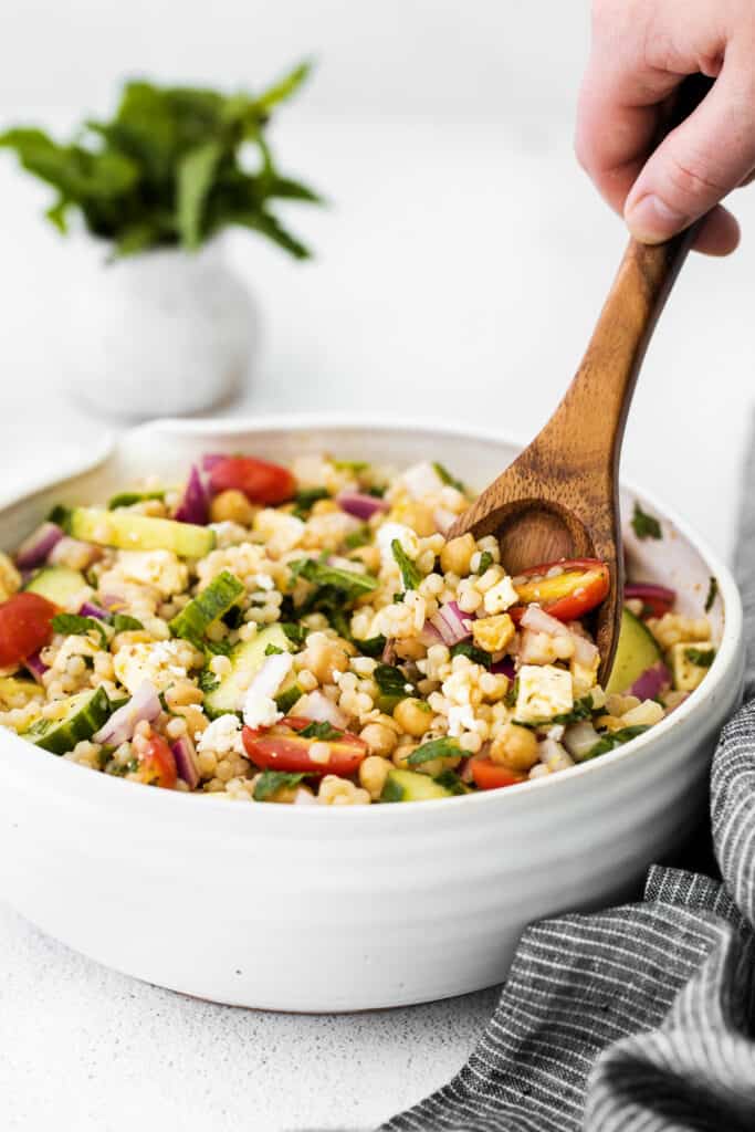 This Mediterranean couscous salad is the perfect addition to any summer meal. Serve this veggie-packed salad as a delicious side dish or a colorful main dish. Enjoy! mediterranean couscous salad in a bowl being stirred with a spoon