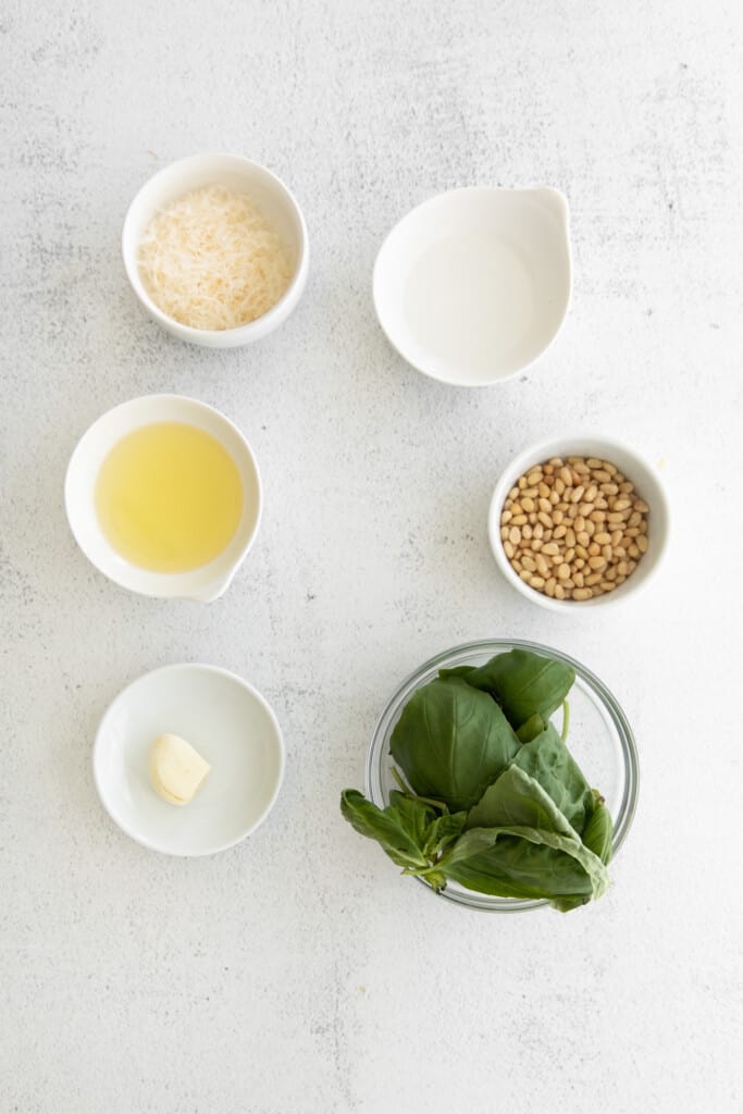 This basil pesto comes together in less than 5 minutes. It's made with fresh basil, garlic cloves, olive oil, parmesan cheese, and pine nuts. ingredients on countertop