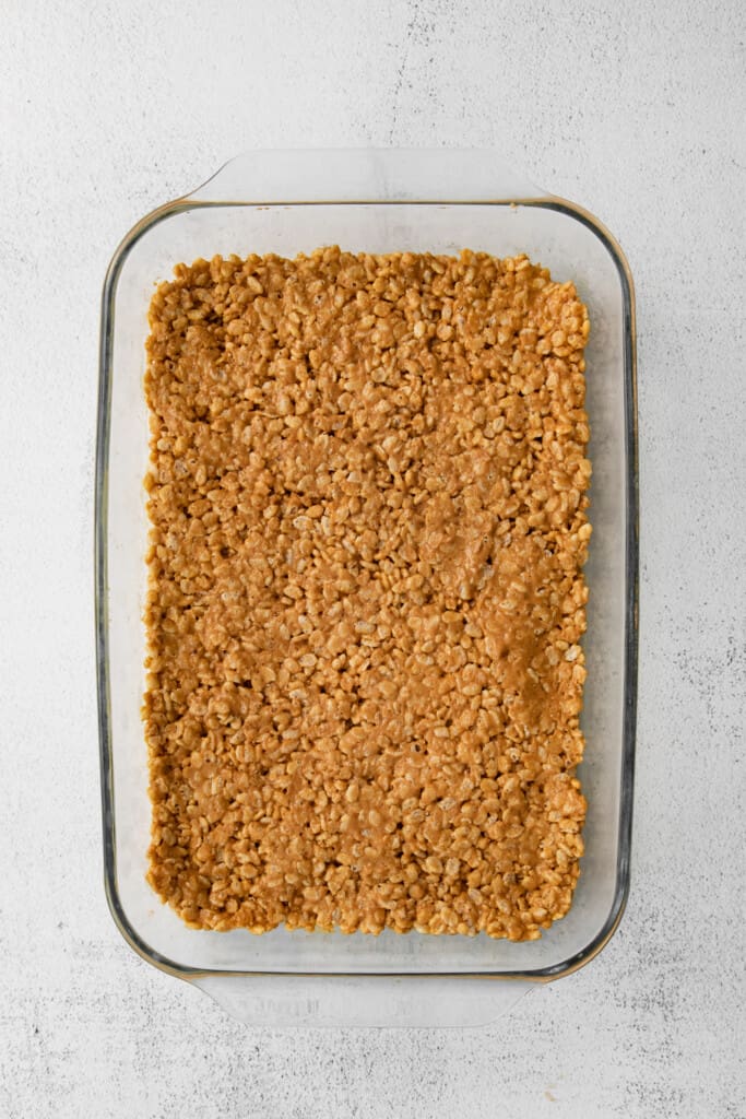 These healthy scotcheroos are made with all natural sugar, unsalted peanut butter, and coconut oil (no white sugar or corn syrup)! They are ready in no time and a great healthy spin on this classic dessert bar. rice crispy layer of healthy scotcheroos in a baking dish