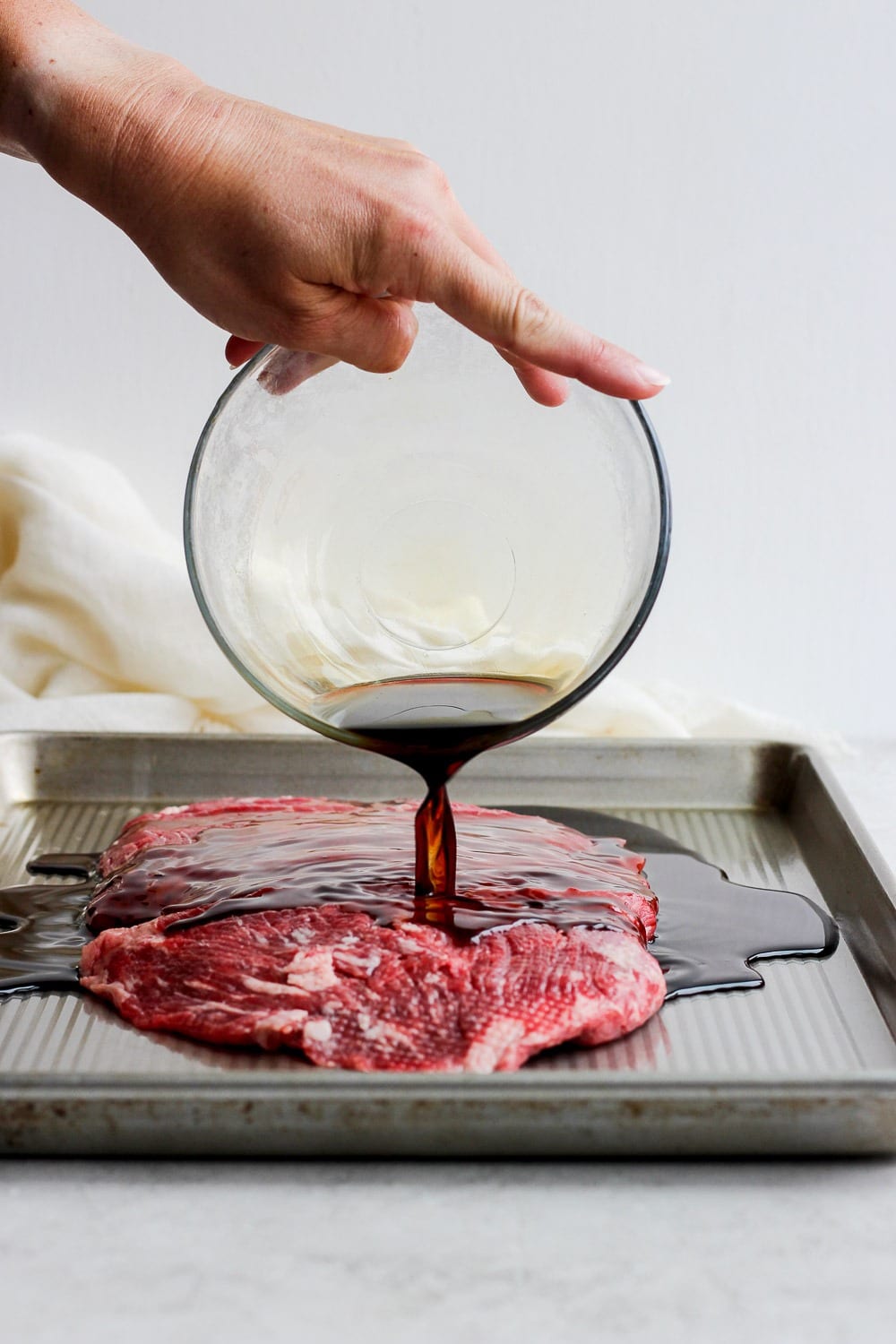 For a more flavorful grilled flank steak, marinate the meat in a delicious soy sauce marinade! You won't regret it! Pouring marinade over flank steak.