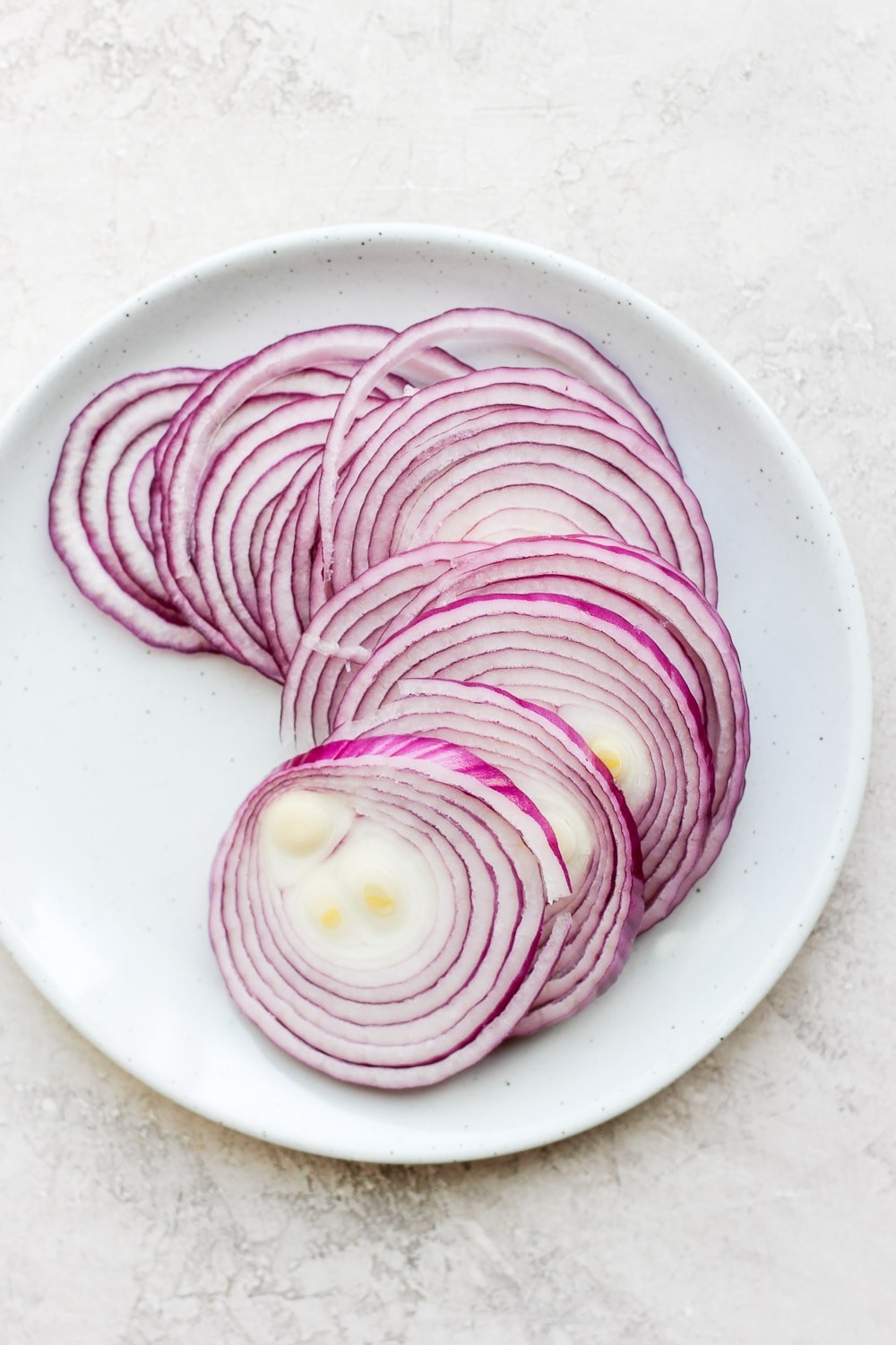 These quick pickled onions are a dream! Toss red onion with apple cider vinegar, white vinegar, a little sugar and salt. Throw them in the fridge and 2 hours later you've got pickled onions for dinner and the week ahead! Raw onions on a plate.