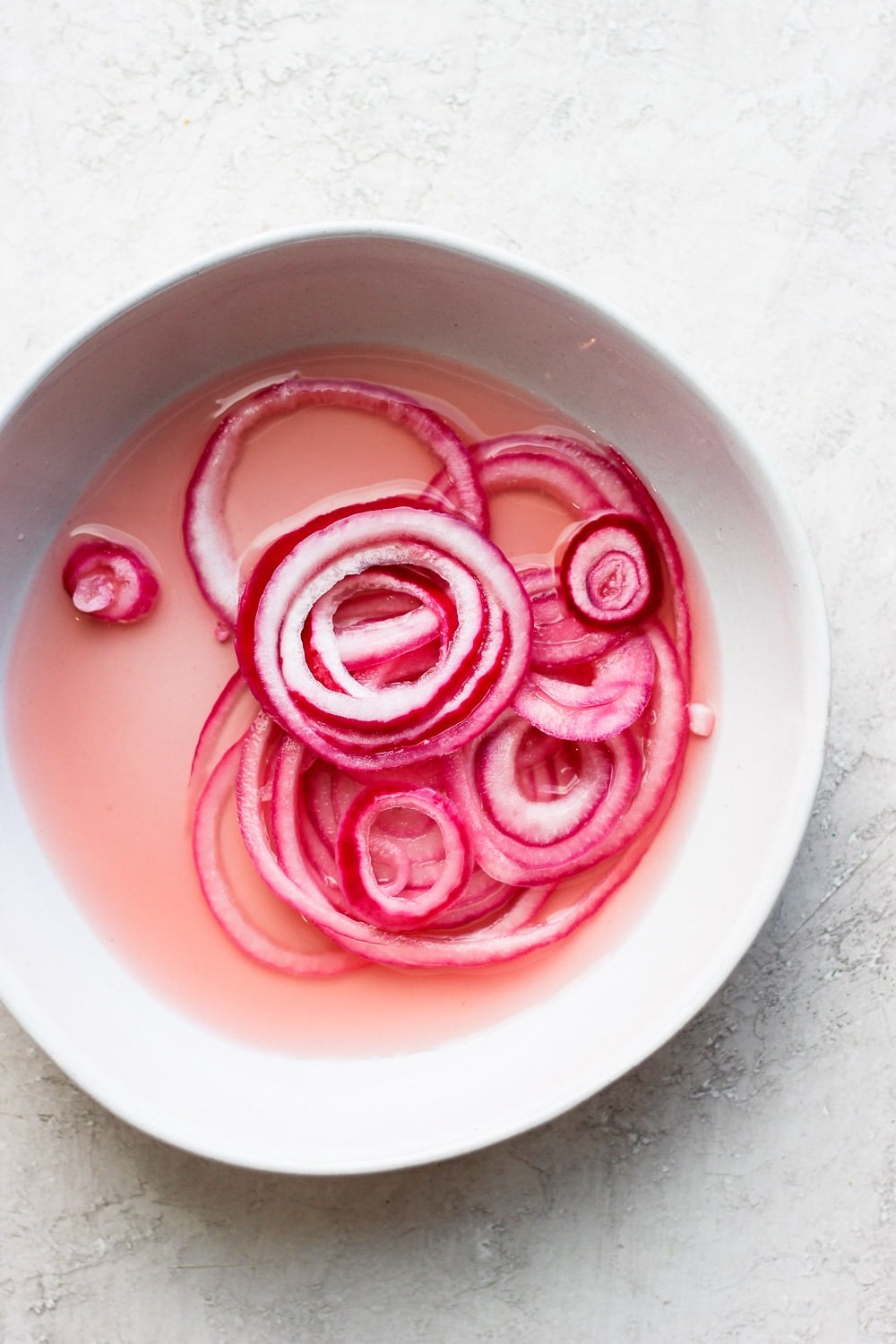 These quick pickled onions are a dream! Toss red onion with apple cider vinegar, white vinegar, a little sugar and salt. Throw them in the fridge and 2 hours later you've got pickled onions for dinner and the week ahead! Pickled onions in a bowl.