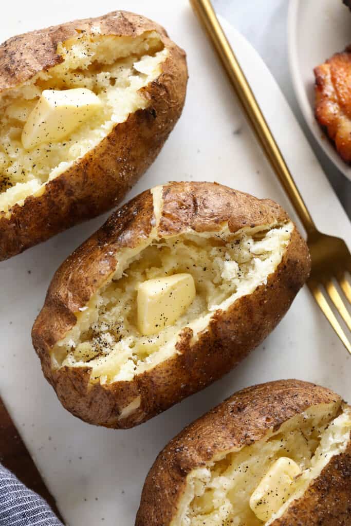 Super simple smoked baked potatoes that'll give you fork tender baked potatoes every time. baked potatoes with cutting board and butter