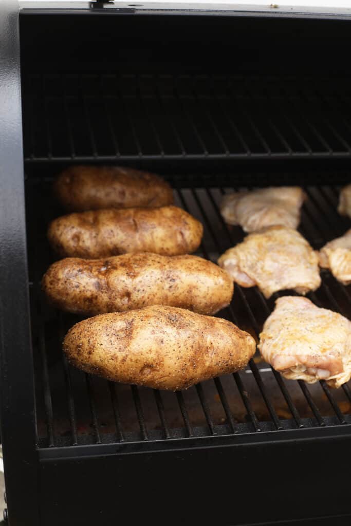 Super simple smoked baked potatoes that'll give you fork tender baked potatoes every time. baked potatoes on smoker with chicken thighs