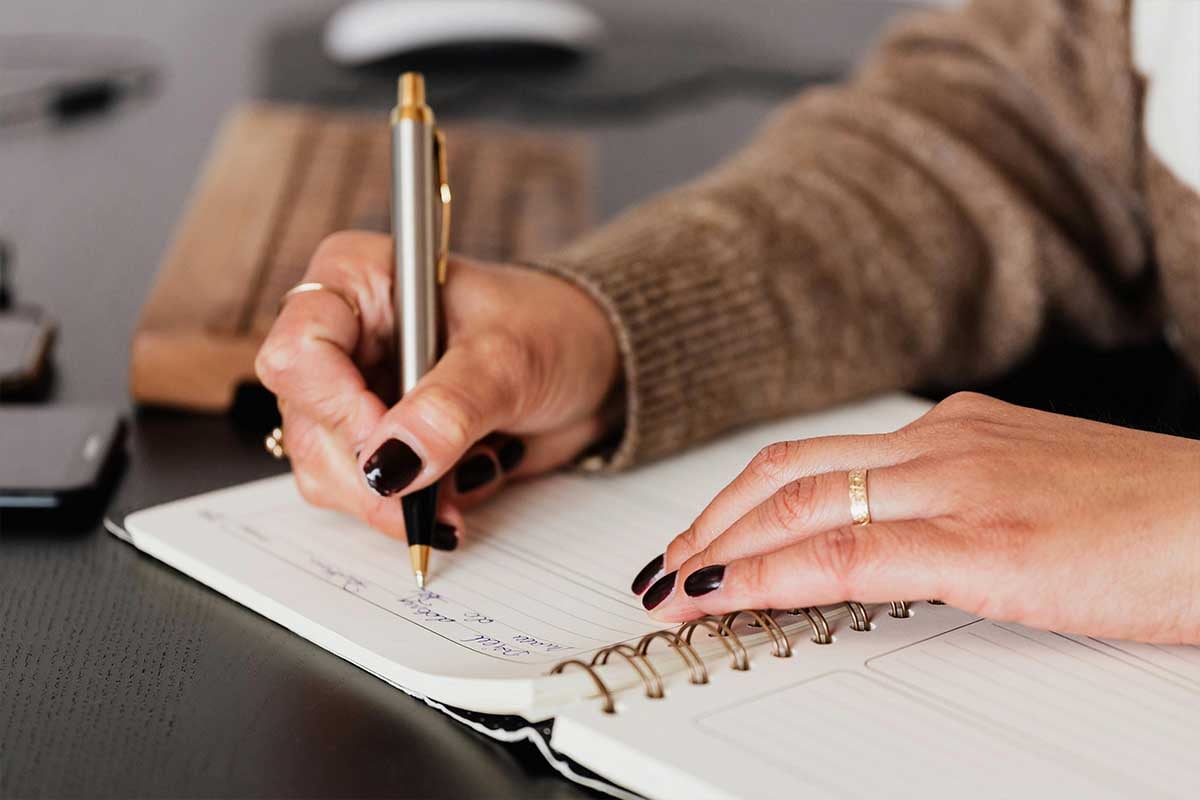 Woman with painted nails writing in a notebook